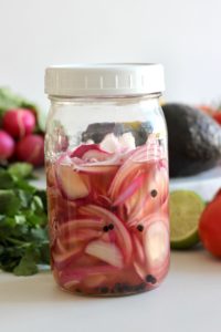 jar of red pickled onions with cilantro and avocado in the background