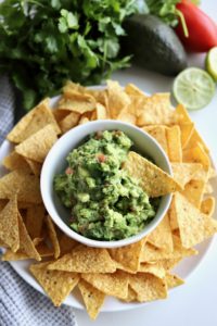 bowl of homemade green guacamole surrounded by tortillas chips